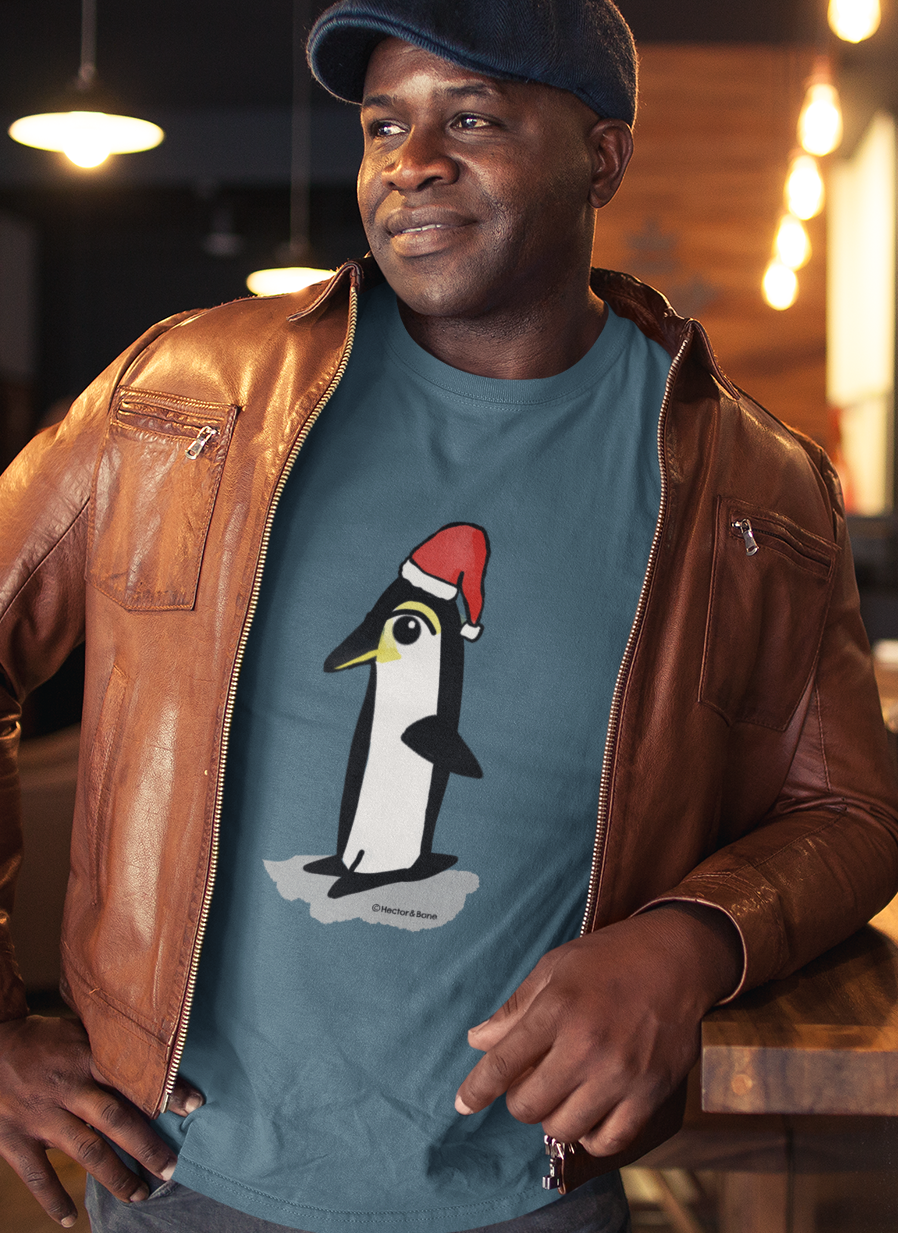 Christmas Penguin T-shirt - Man at a Christmas party wearing a Santa Penguin cute Christmas T-shirt in stargazer blue colour illustrated design by Hector and Bone on a Vegan cotton t-shirt