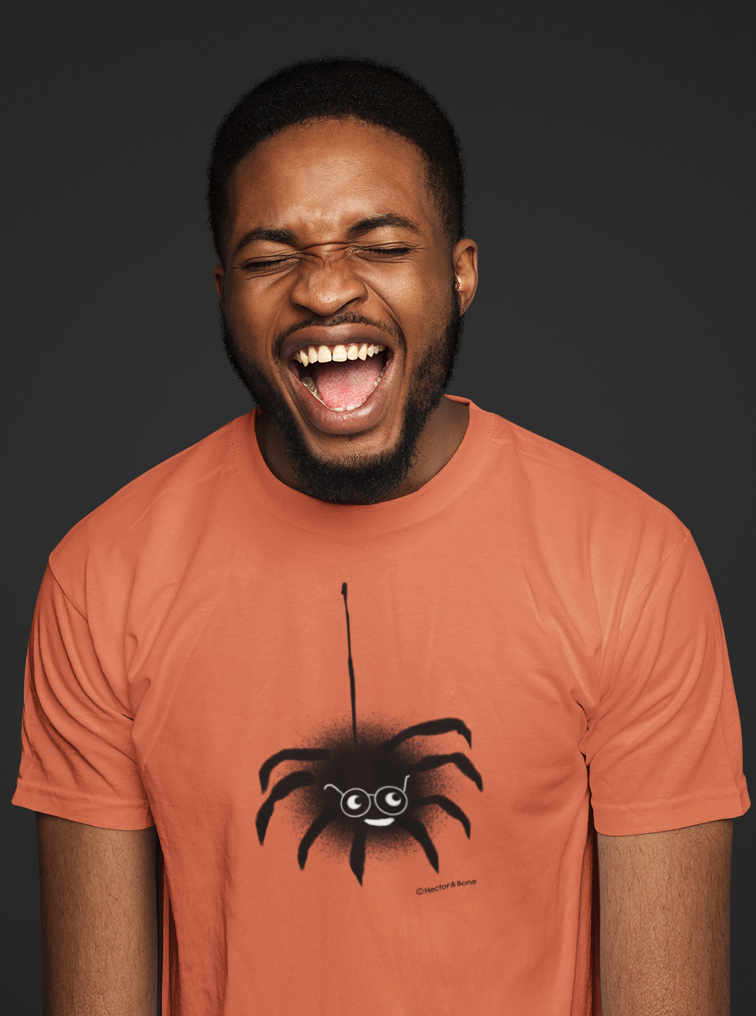 Spider T-shirt - A young man laughing wearing a cute Spectacled Spider original illustrated Halloween design on a Hector and Bone quality vegan orange colour cotton t-shirt