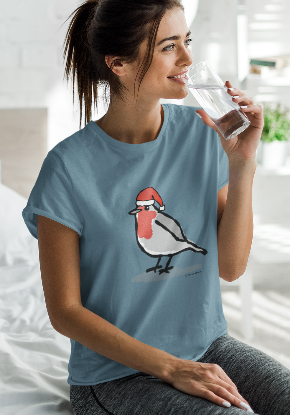 Young woman relaxing at Xmas, wearing a illustrated Santa Christmas Robin T-shirt - Stargazer Blue colour vegan cotton Christmas T-shirts by Hector and Bone