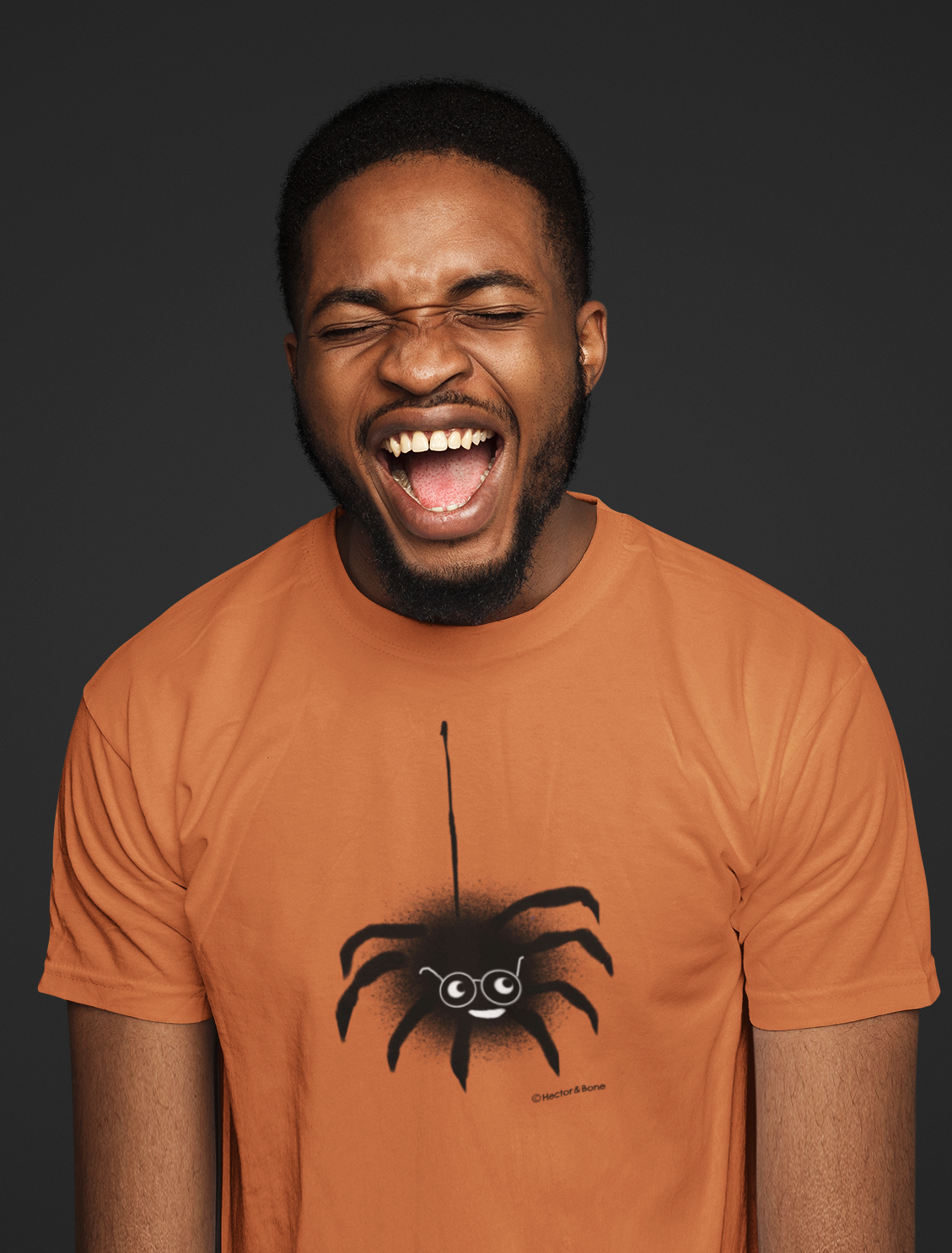 Spider T-shirt - A young man laughing wearing a cute Spectacled Spider original illustrated Halloween design on a Hector and Bone quality vegan pumpkin orange colour cotton t-shirt