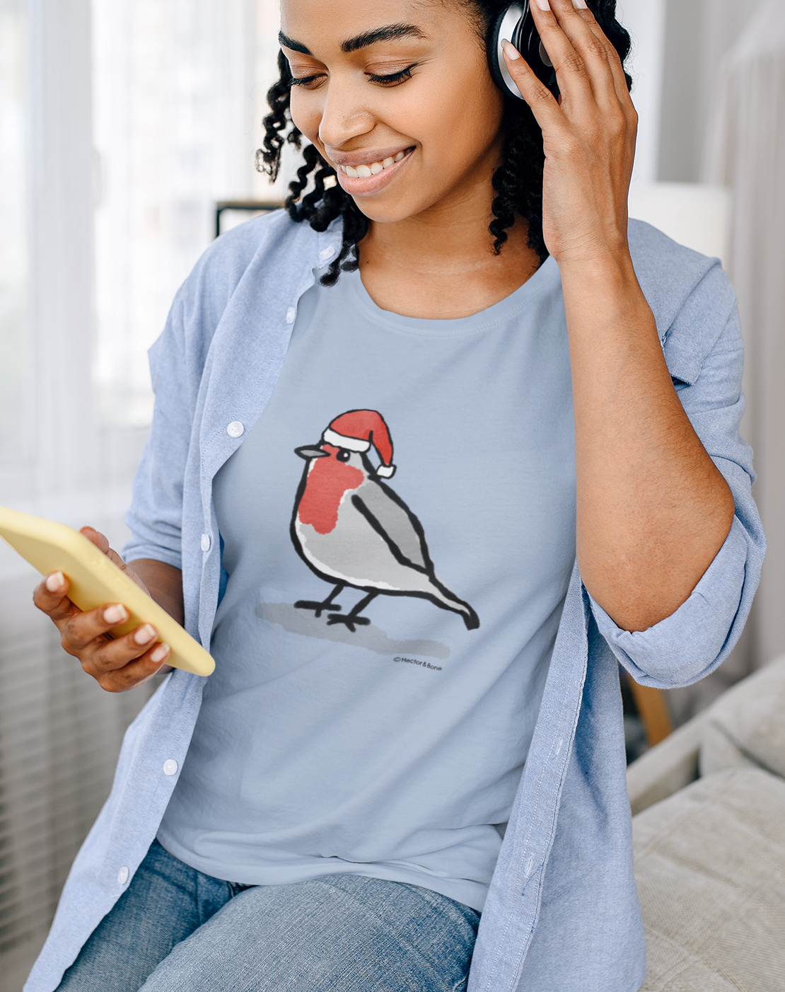 Young woman relaxing at Xmas, wearing a illustrated Santa Christmas Robin T-shirt - Sky Blue colour vegan cotton Christmas T-shirts by Hector and Bone