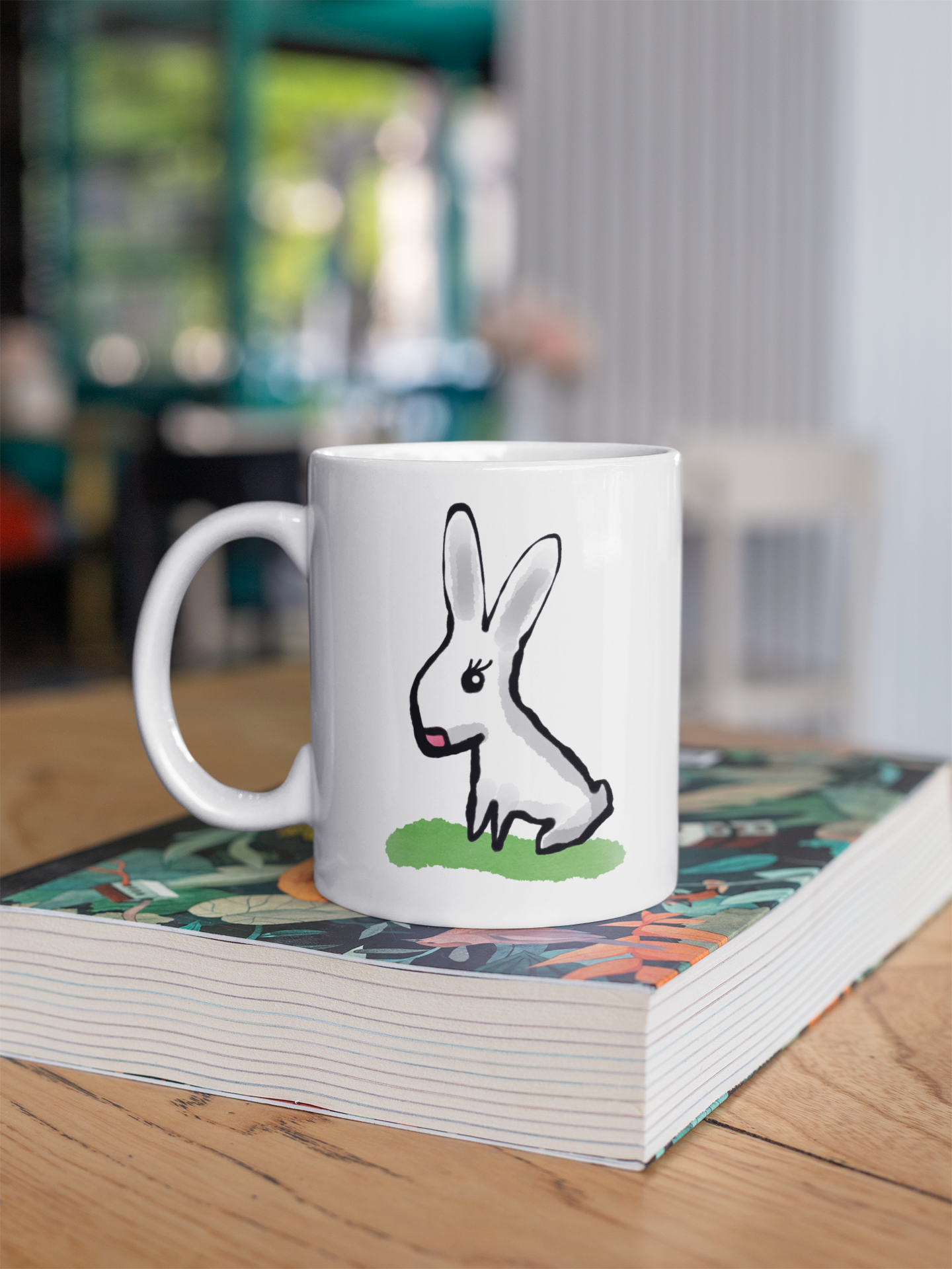 Cute Bunny coffee mug illustration by Hector and Bone - sitting on a book at home