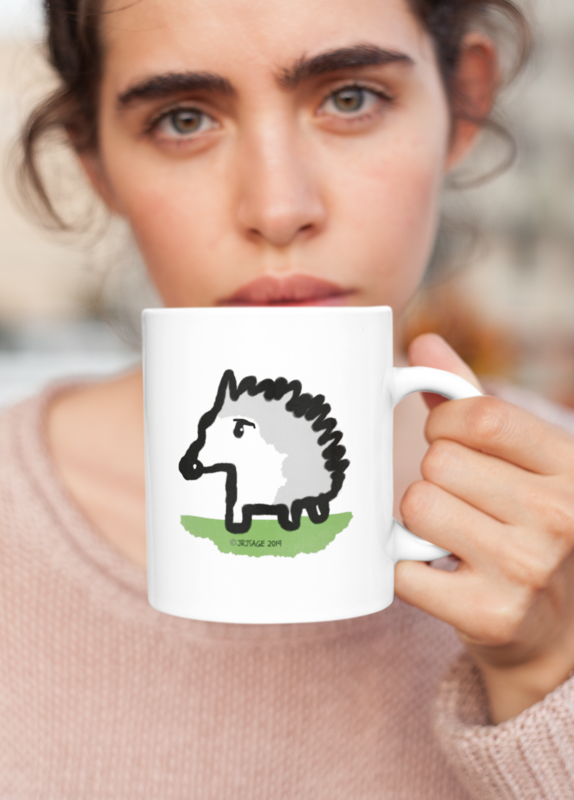 A woman sipping from a White Ceramic Hector and Bone Mug with an illustration of a cute Baby Hedgehog