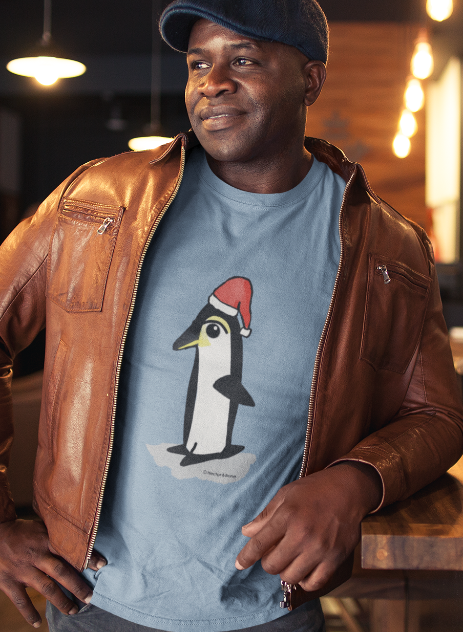 Christmas Penguin T-shirt - Man at a Christmas party wearing a Santa Penguin cute Christmas T-shirt in mid heather blue colour illustrated design by Hector and Bone on a Vegan cotton t-shirt