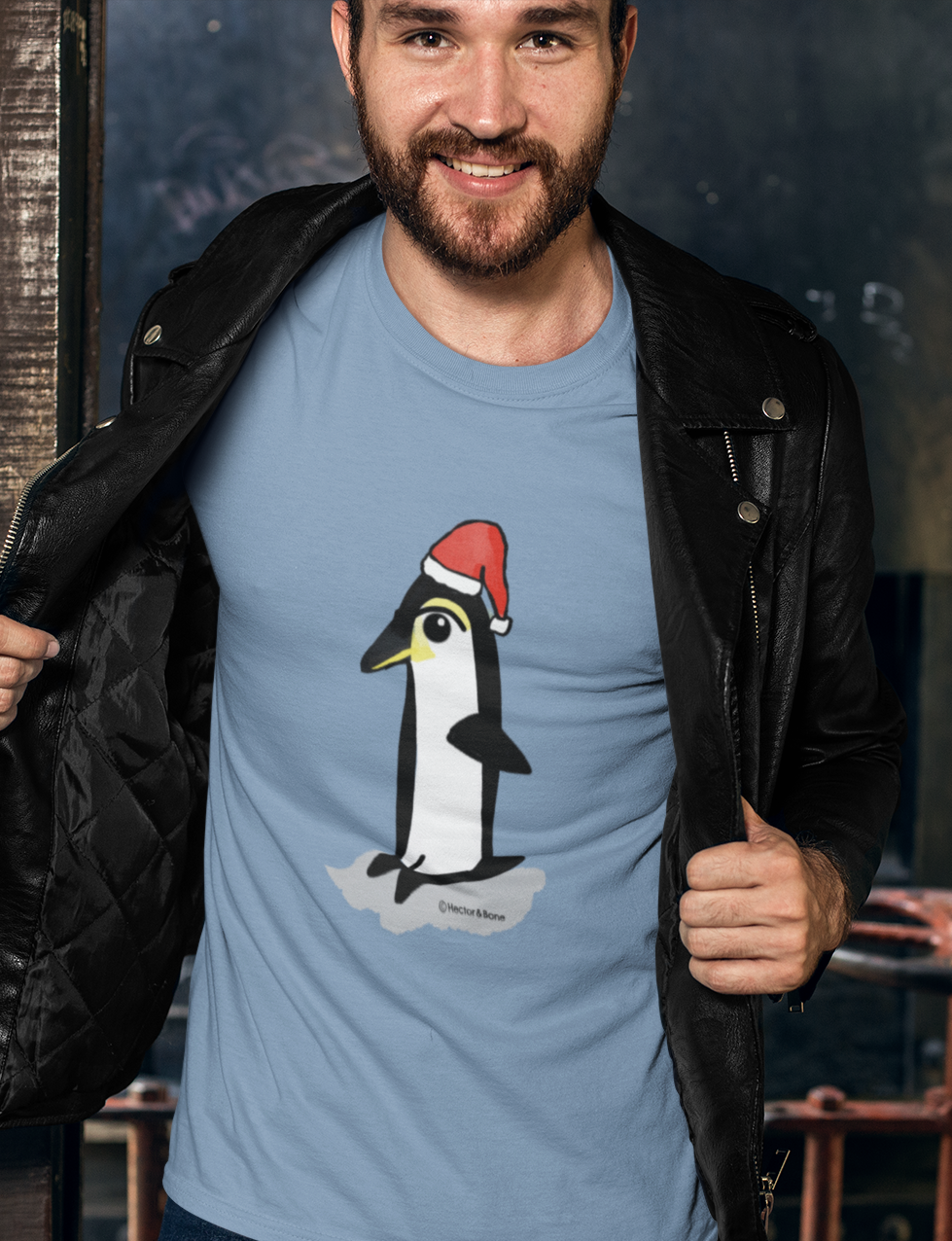 Christmas Penguin T-shirt - Young man at a Christmas party wearing a Santa Penguin cute Christmas T-shirt in mid heather blue colour illustrated design by Hector and Bone on a Vegan cotton t-shirt
