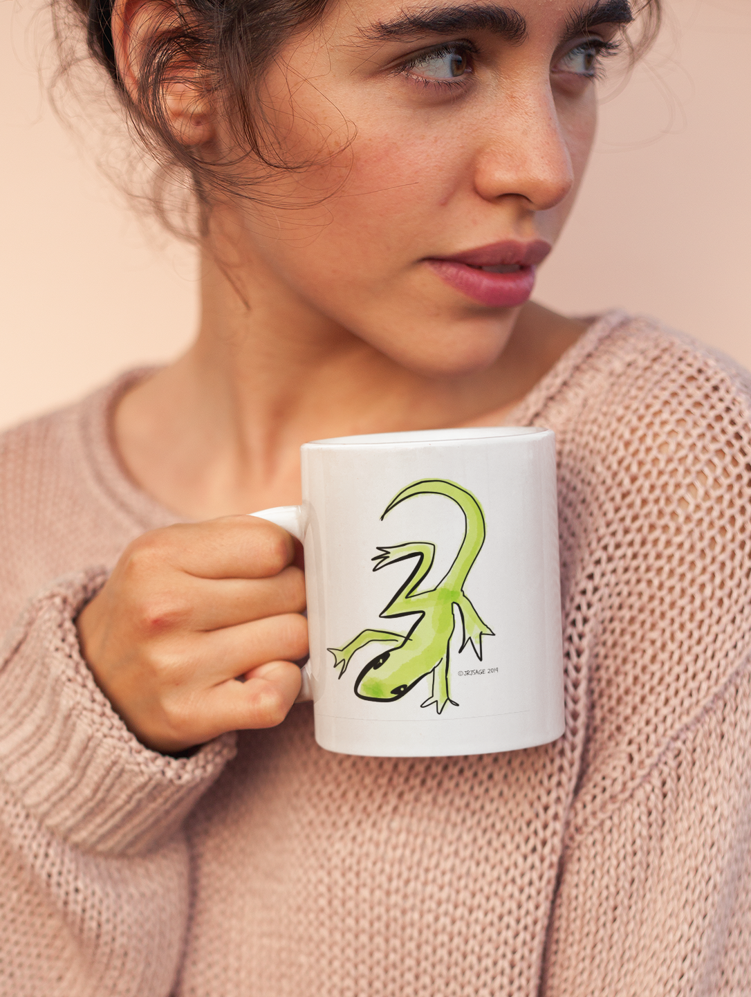 Young woman holding a ceramic white Hector and Bone mug with a Green Lizard illustration