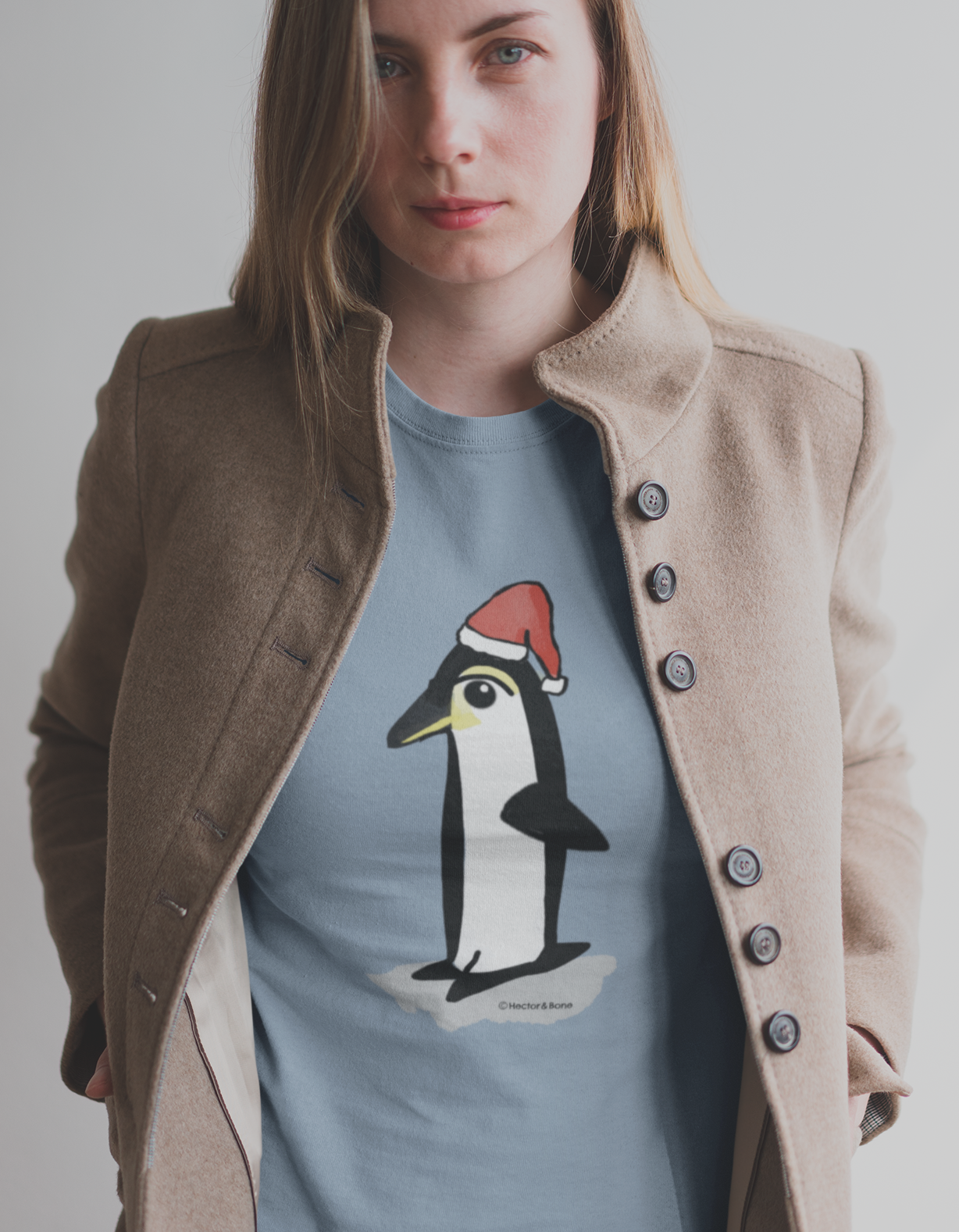 Christmas Penguin T-shirt - Young woman wearing a Santa Penguin cute Christmas T-shirt in mid heather blue colour illustrated design by Hector and Bone on a Vegan cotton t-shirt