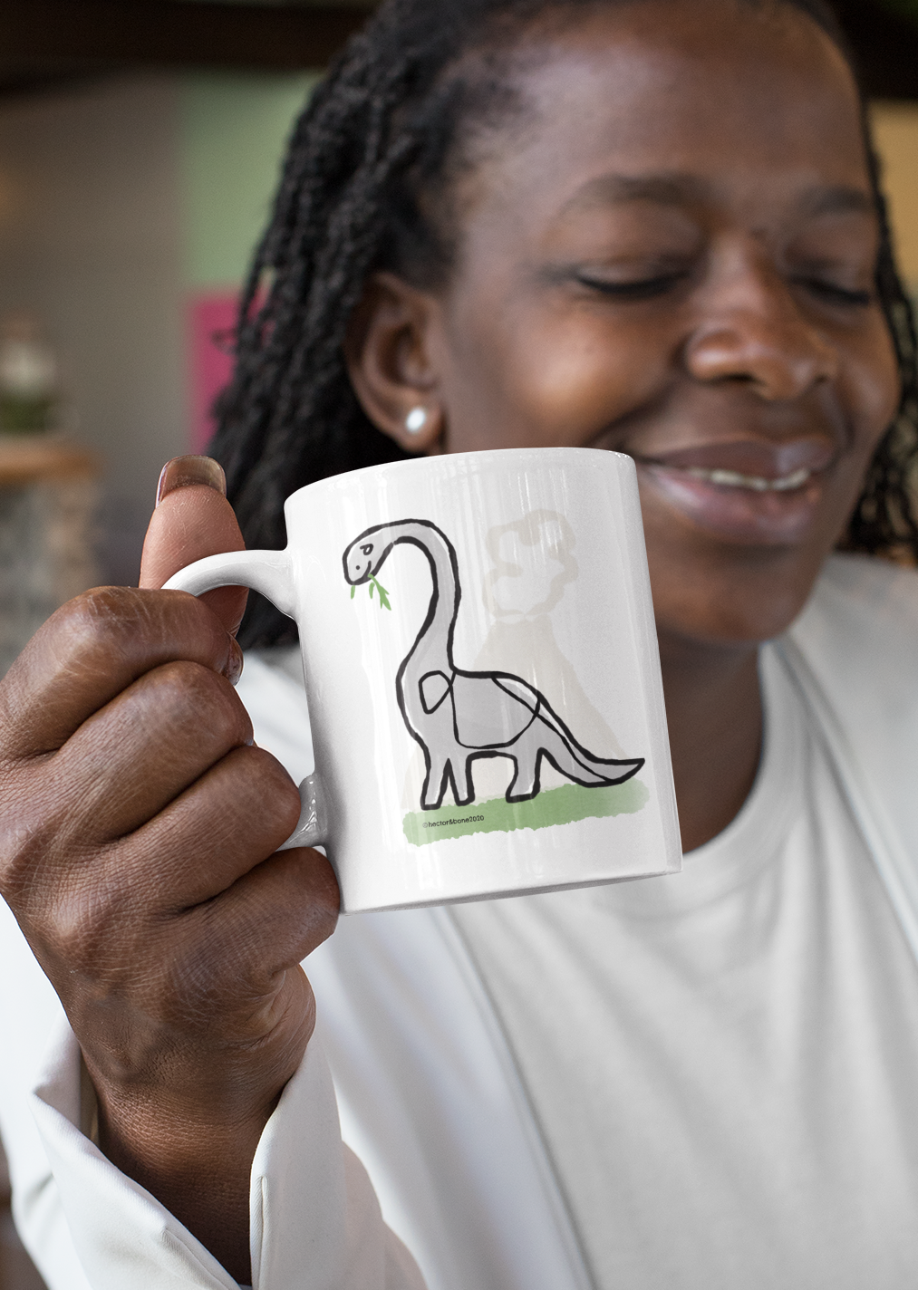 A woman holding a cute Derek Dinosar illustrated Brontosaurus ceramic coffee mug by Hector and Bone