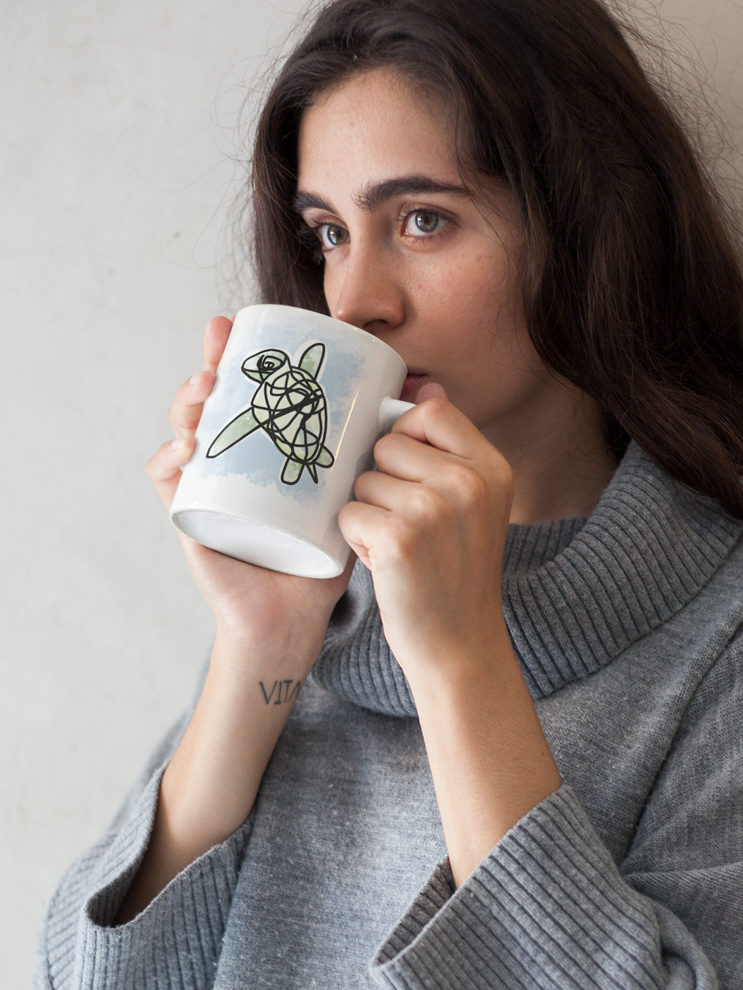 A young woman holding a Myrtle the Sea Turtle illustrated ceramic coffee mug by Hector and Bone